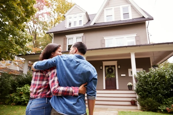 Couple embracing as they stand in front of their new home.