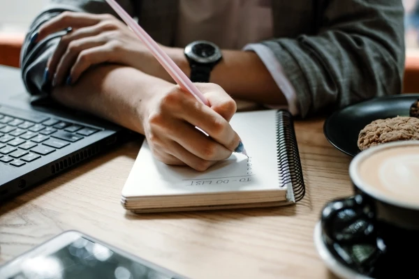 Person sitting at a desk writing out a project ‘to do’ list