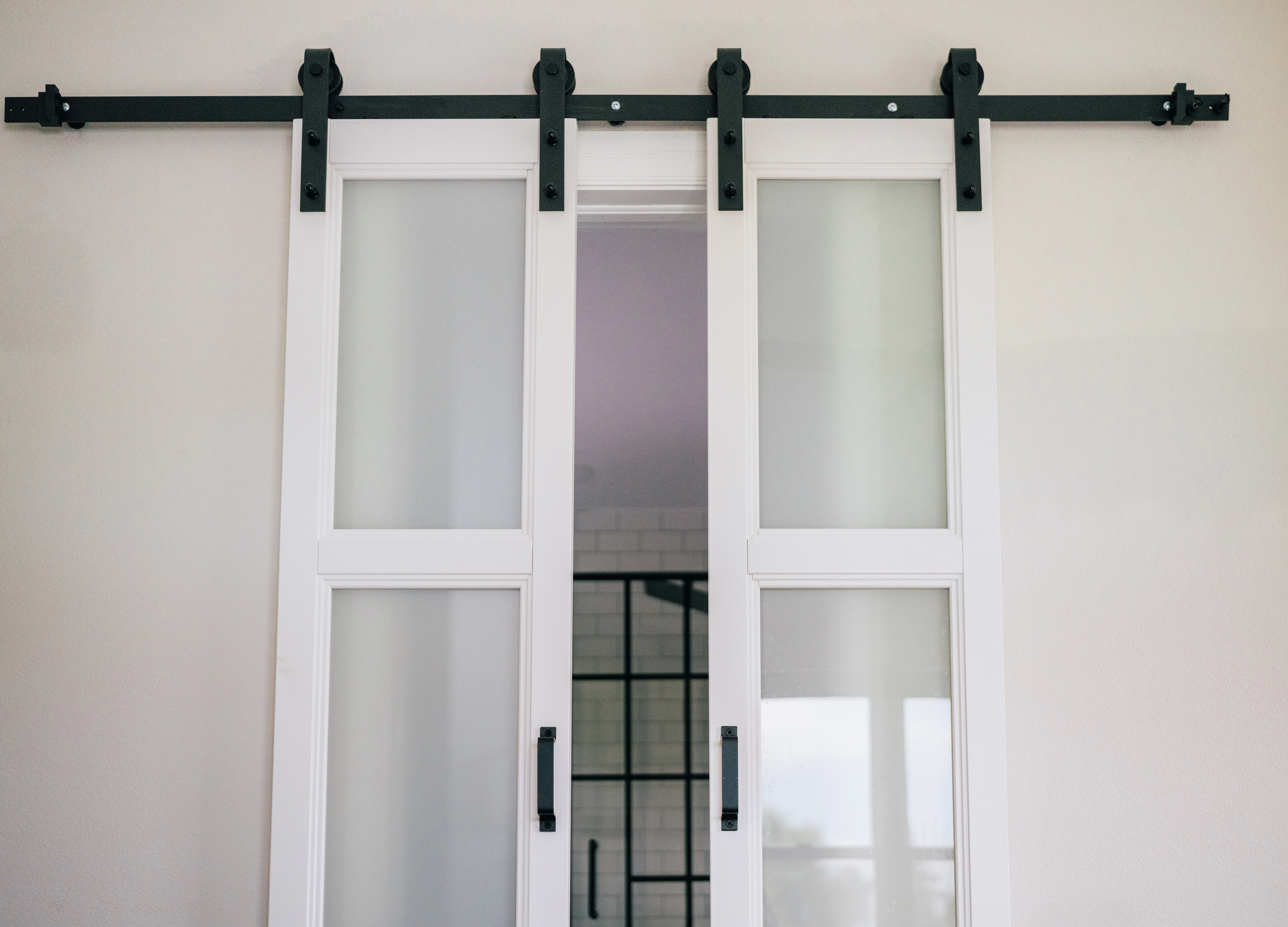 Close-up of white painted split barn door with black metal slider opening up to interior bathroom.