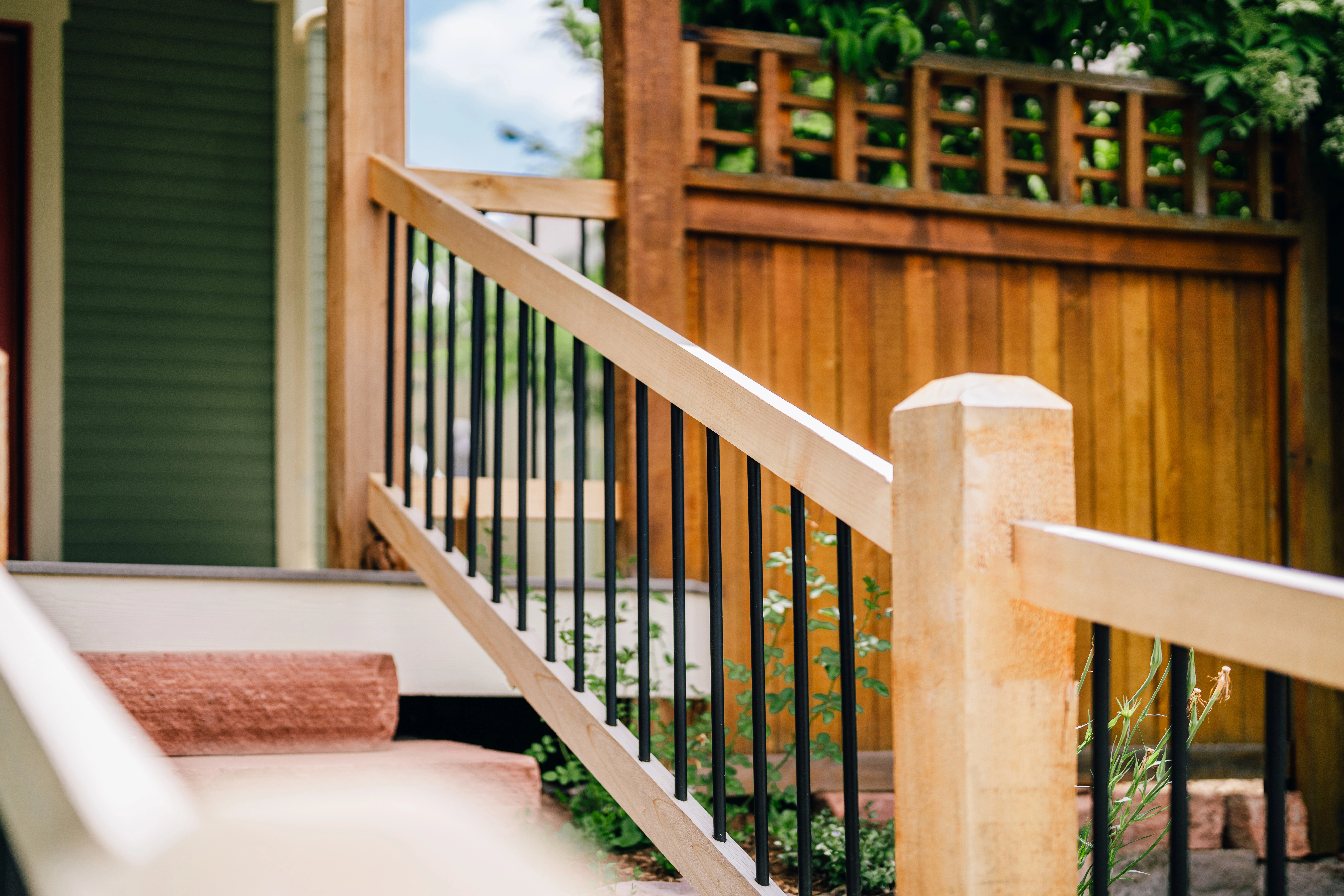 Close-up of unstained light wood exterior railing leading up front steps to a deck.