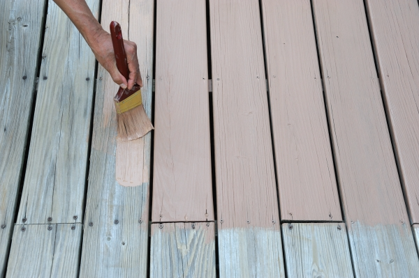Person using a paint brush to paint a wooden deck