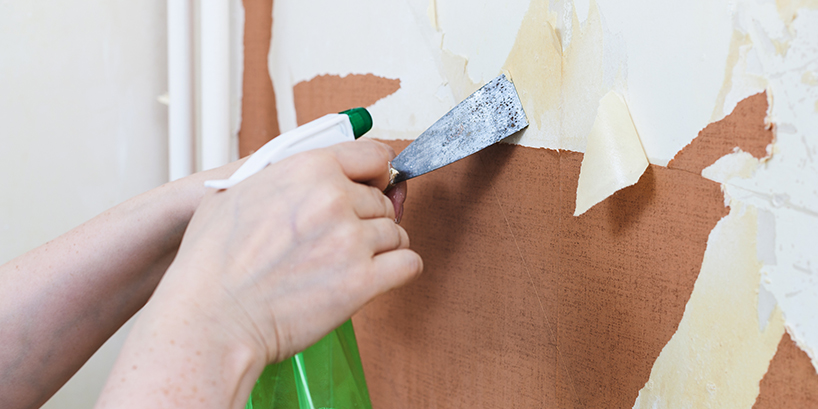 Photo of someone removing wallpaper with a metal scraper and a spray bottle
