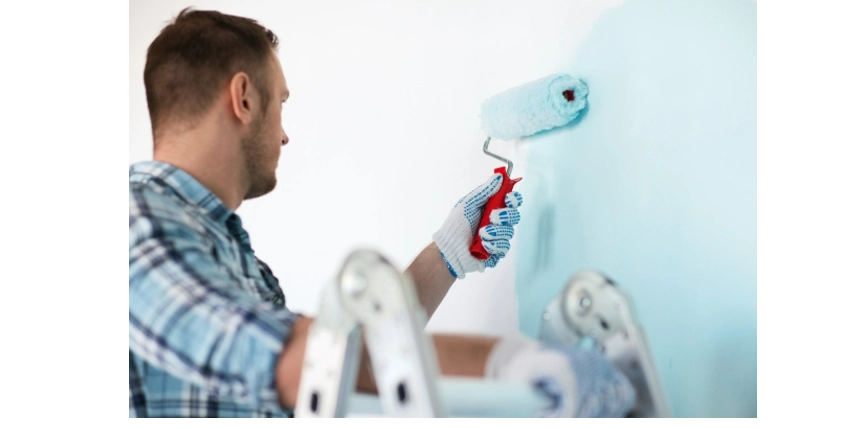 Man wearing work gloves and using a roller to paint an interior wall.