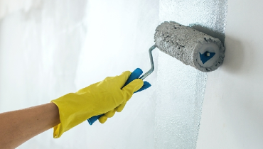 Person wearing yellow rubber glove using a paint roller to paint an interior wall