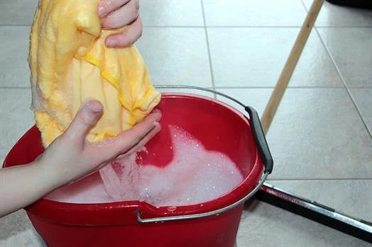 Hands holding soapy yellow cloth over a red bucket full of soapy water