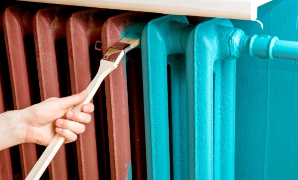 Closeup of a person using a special curved paint brush to paint a radiator.