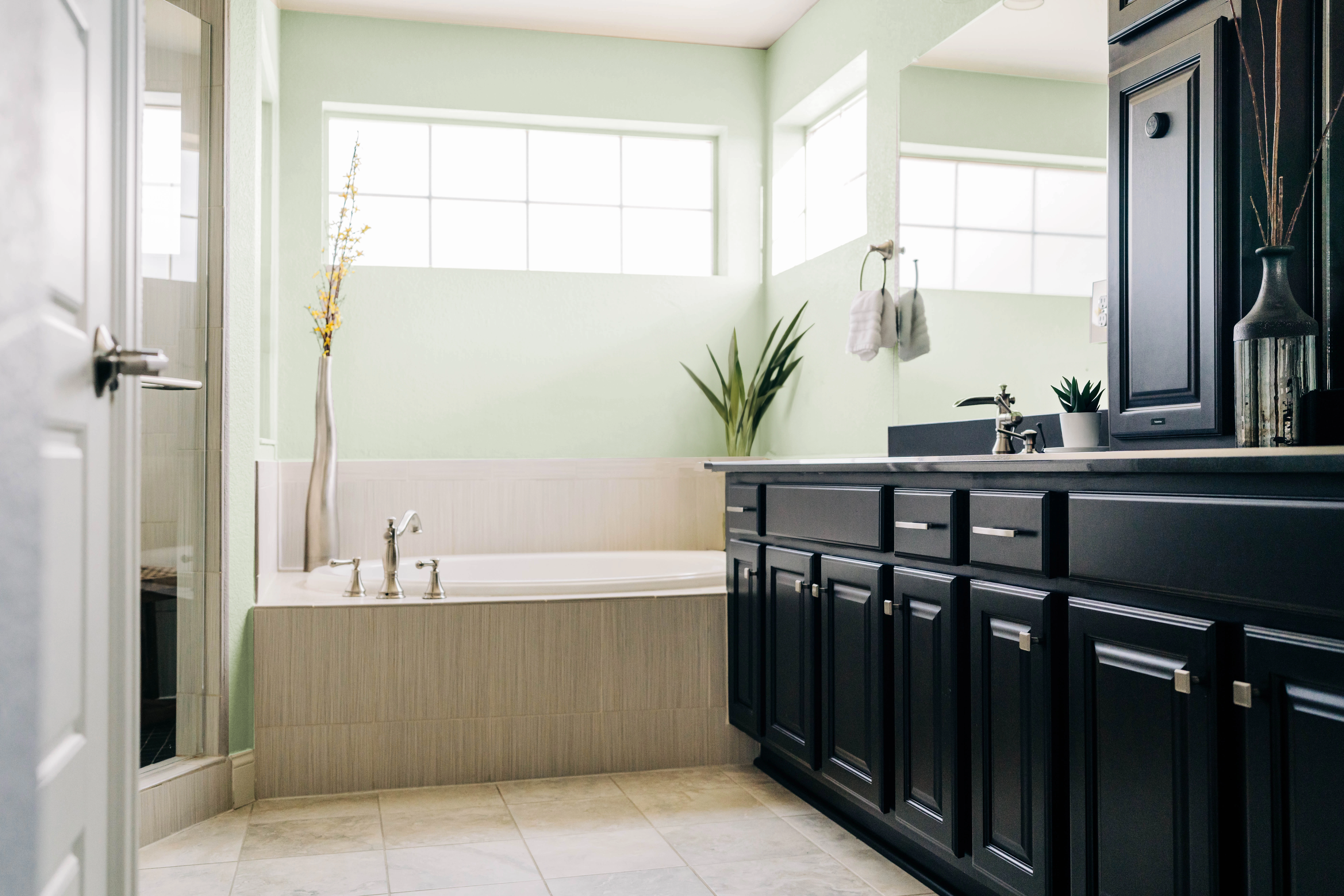 Built-in tub bathroom with light green walls, black built-in sink cabinets, and a corner shower. 