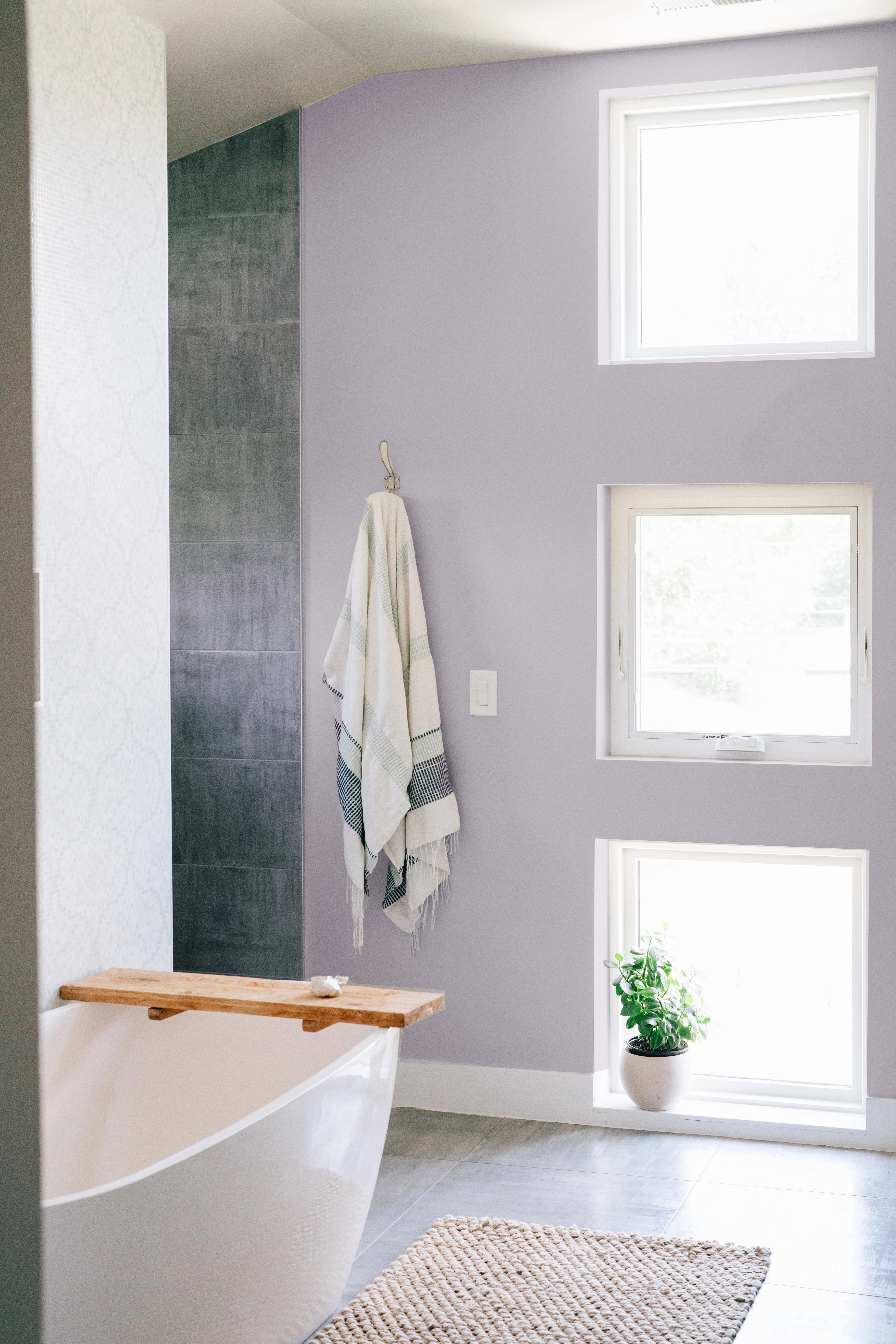 Light gray-blue painted bathroom with freestanding tub and three bright windows.