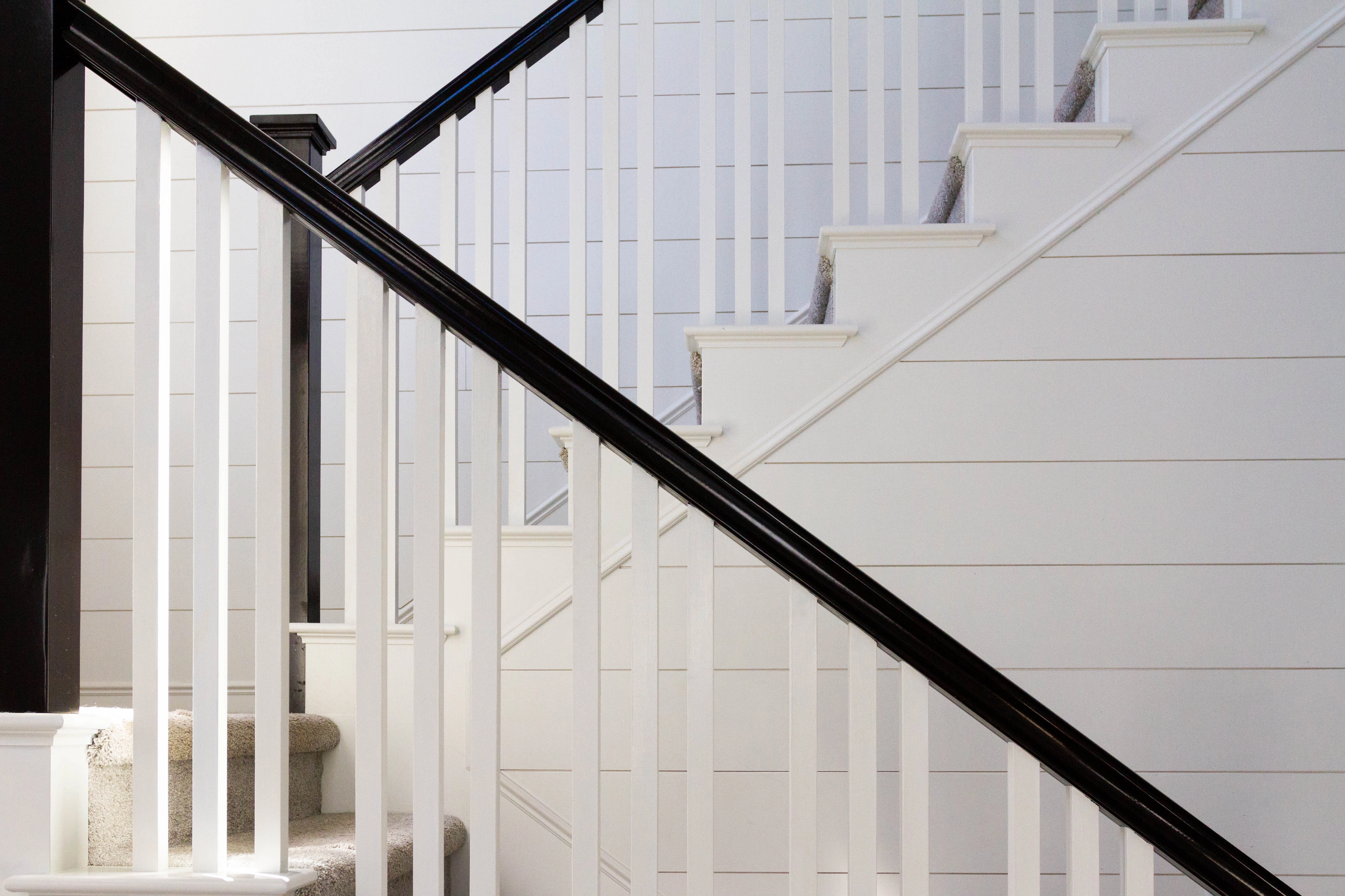 Carpeted half turn stairs with white paneled risers and walls, and black railing and post.