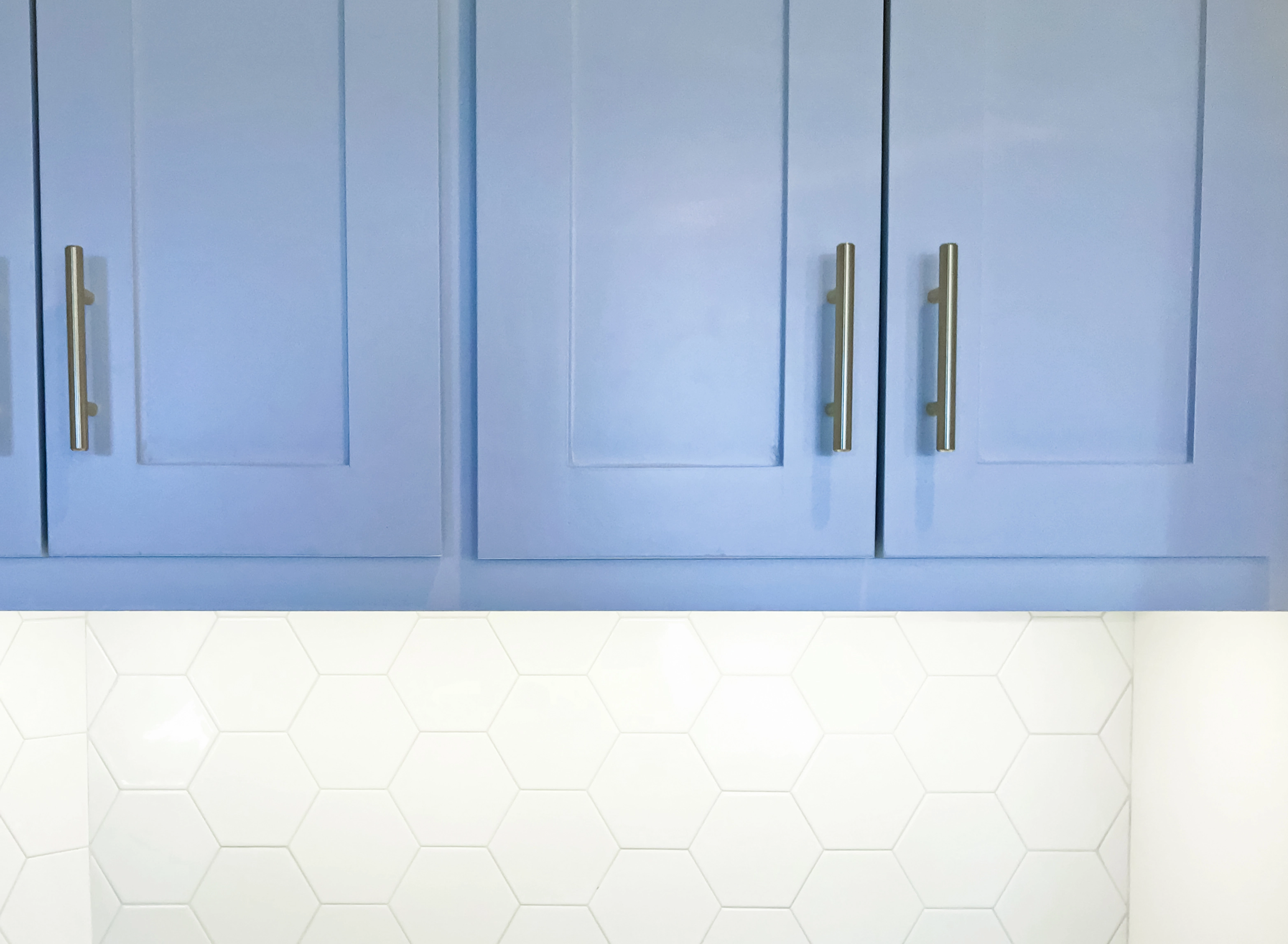 Close-up of cornflower blue painted cabinets with white hexagon tile on the wall below.
