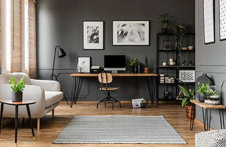 Interior of a office room with wood flooring, grey painted walls, a couch, desk and shelves.