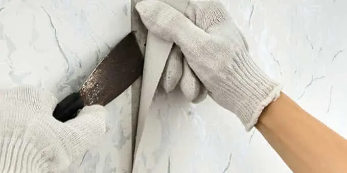 A hand using a tool to remove wallpaper.